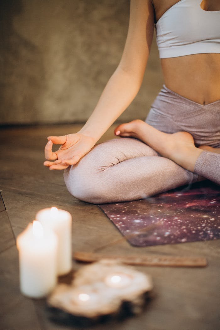 about-us A woman practicing yoga indoors in lotus pose with candles creating a calming atmosphere.